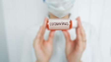 image of a person in a face mask holding a small bottle labeled coronavirus